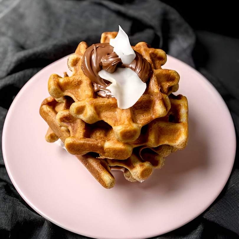 Stack of golden waffles topped with chocolate spread and white coconut flakes on a pink plate.