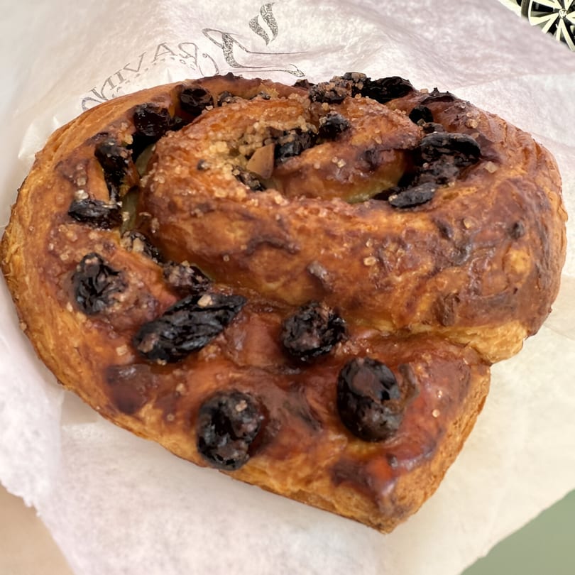 Close-up of a Cravings Coffee & Pastries cinnamon roll with raisins and sugar crystals.