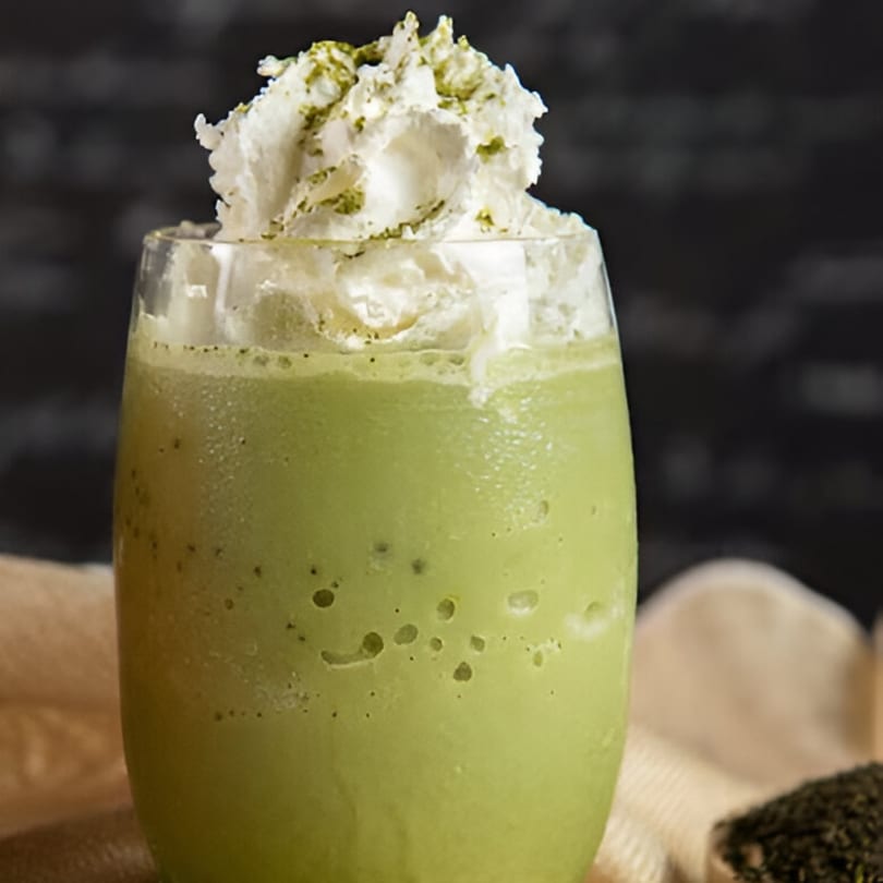 Cravings Coffee & Pastries' vibrant green matcha frappe, topped with whipped cream and a sprinkle of matcha powder.