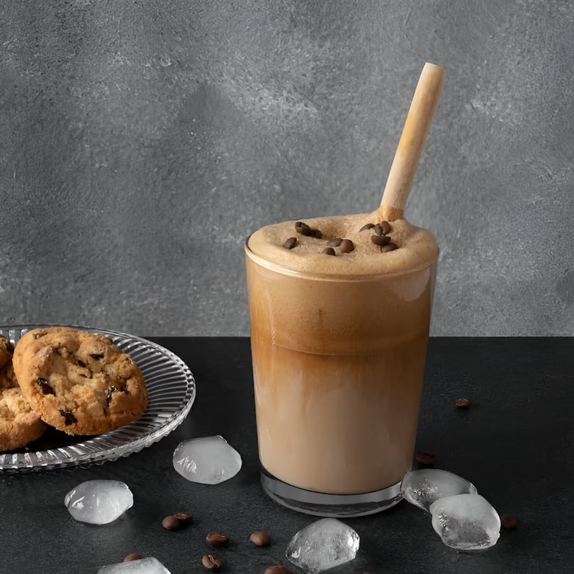 Iced coffee with foam and coffee beans, cookies on a plate, and ice cubes.